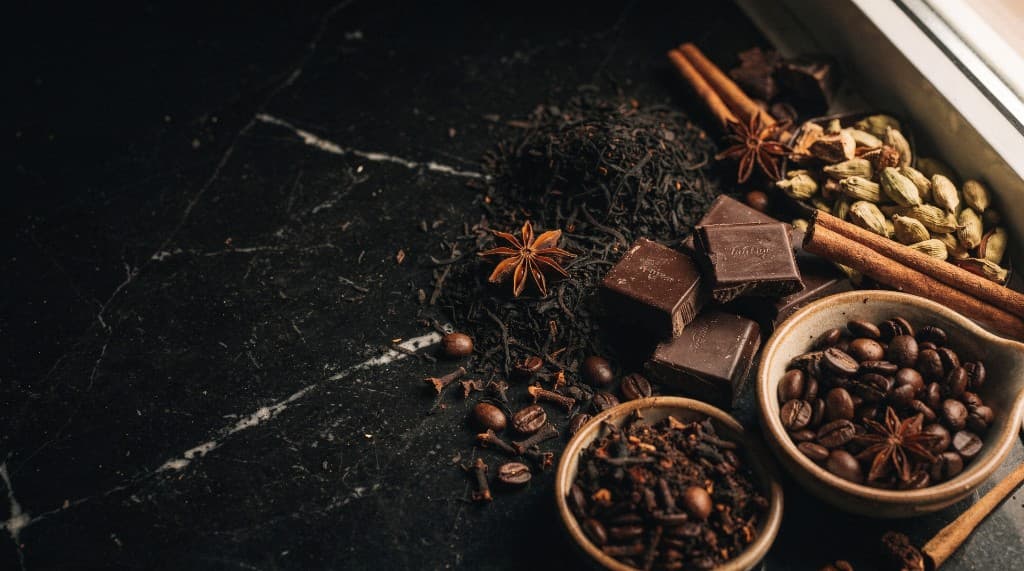 Coffee beans, loose tea, dark chocolate, star anise, cinnamon sticks and cardamom on marble