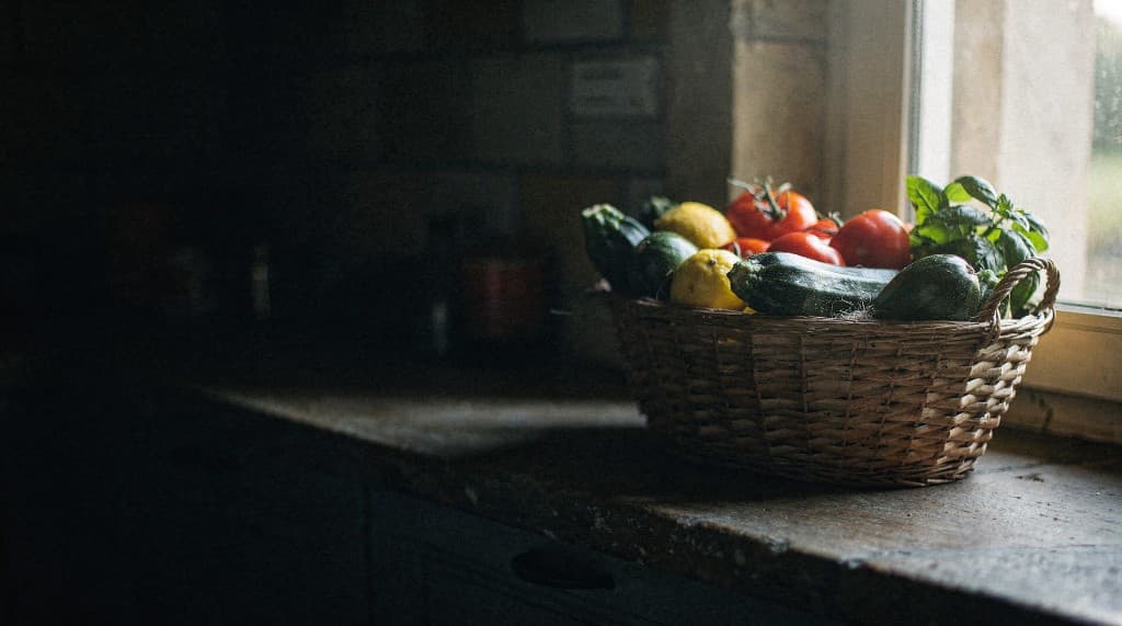 A woven basket of fresh organic tomatoes, zucchini, lemons and basil on a sunlit wooden windowsill
