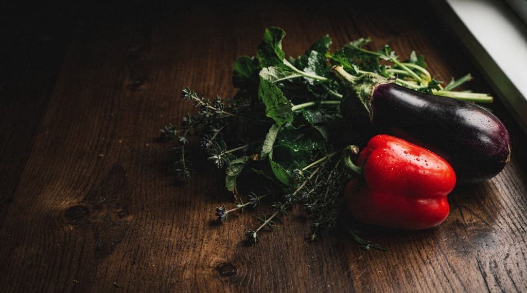 Fresh organic red bell pepper, eggplant and leafy greens with herbs on a dark wooden table
