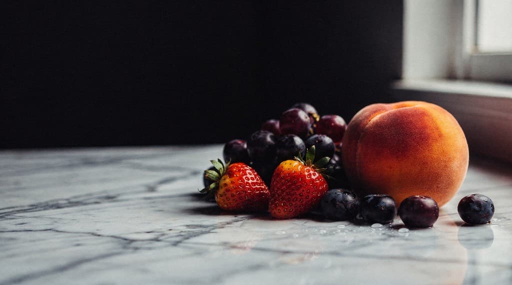 Fresh organic peaches, grapes, strawberries and blueberries on a white marble countertop