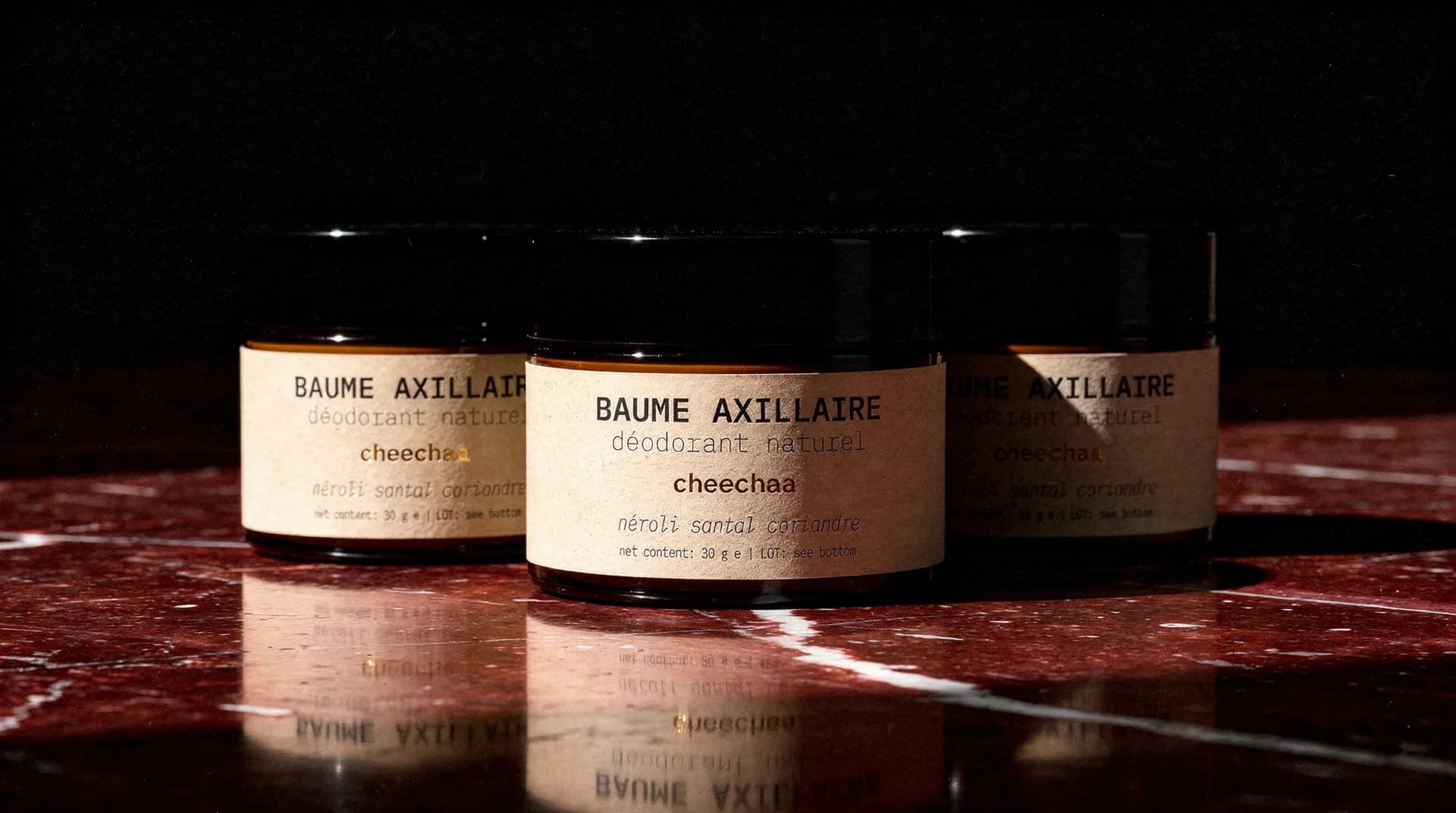 Three jars of BAUME AXILLAIRE on red marble