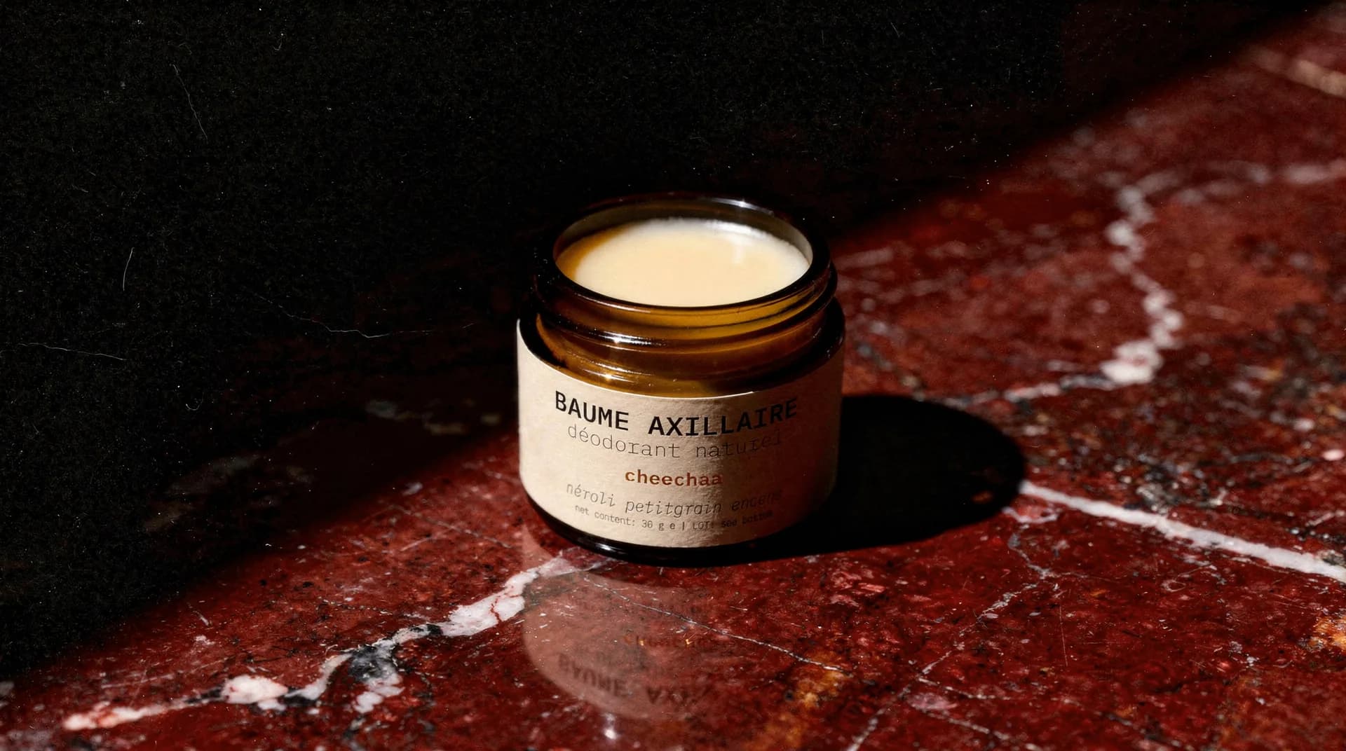 Open jar of BAUME AXILLAIRE néroli petitgrain encens on red marble